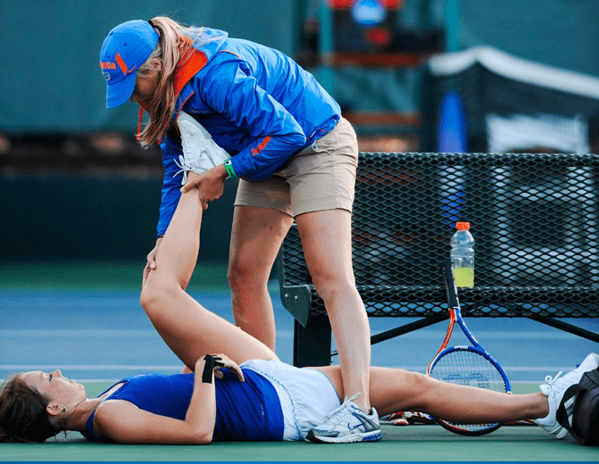 Two female tennis players are stretching their legs.